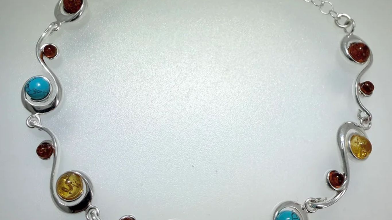 A silver bracelet with amber and turquoise stones in a swirling design.